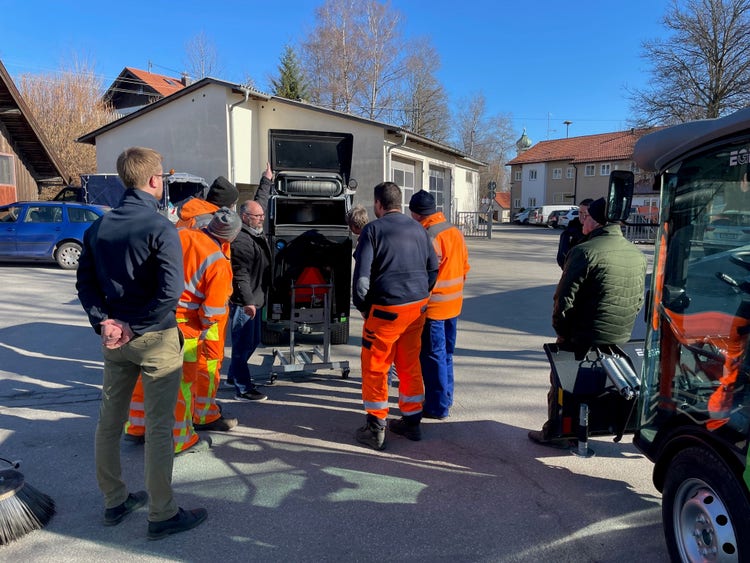 Einige Männer in orangener Uniform stehen um eine Egholm Kehrmaschine