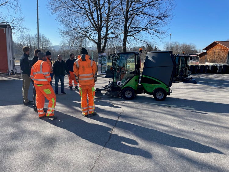 Einige Männer in orangener Uniform stehen um eine Egholm Kehrmaschine