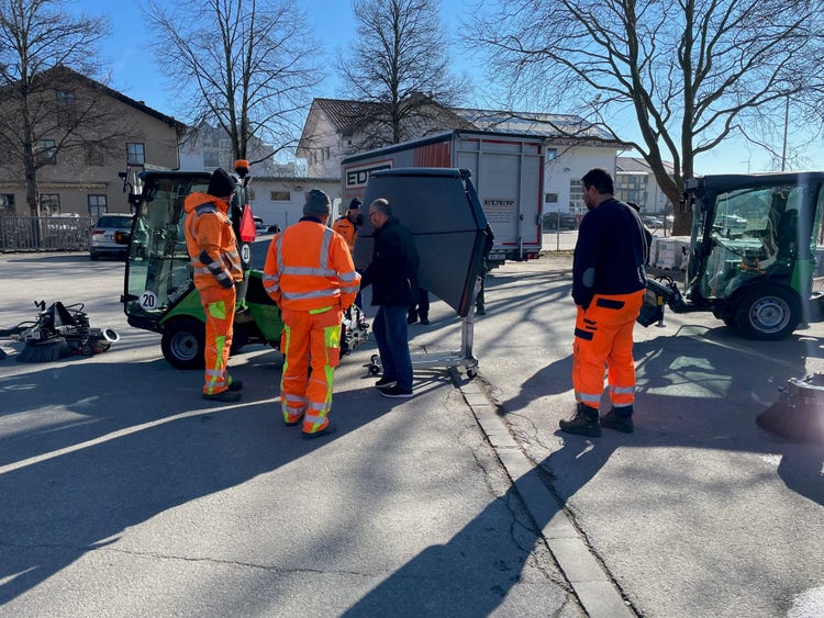 Einige Männer in orangener Uniform stehen um eine Egholm Kehrmaschine
