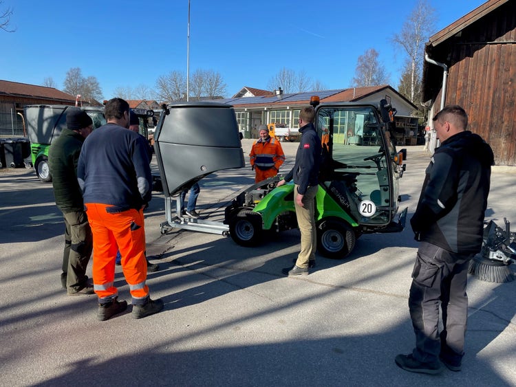 Einige Männer in orangener Uniform stehen um eine Egholm Kehrmaschine