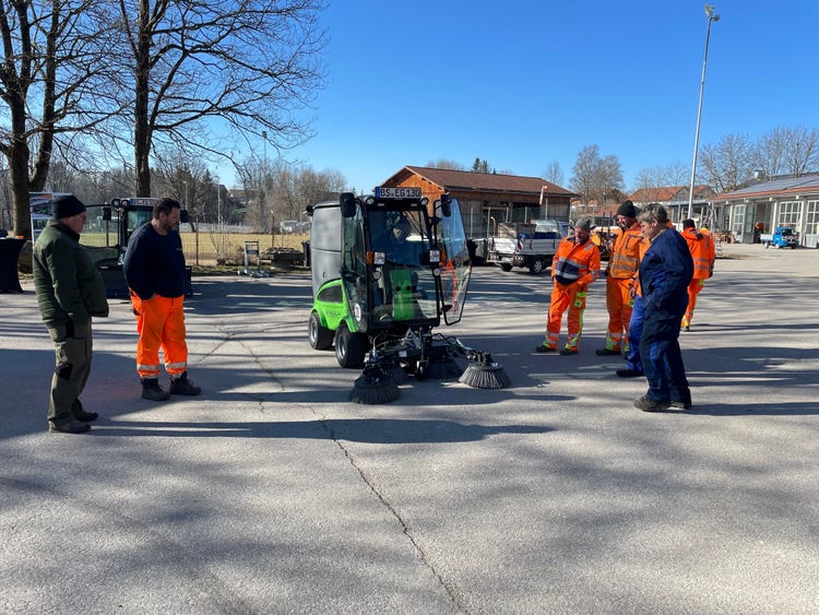 Einige Männer in orangener Uniform stehen um eine Egholm Kehrmaschine
