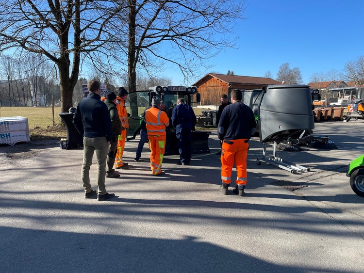 Einige Männer in orangener Uniform stehen um eine Egholm Kehrmaschine
