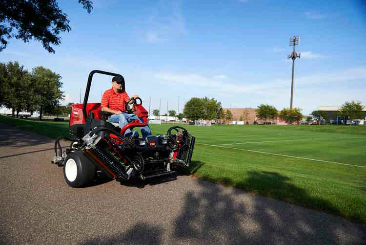 Ein Mann fährt mit dem Toro Reelmaster 3575-D auf einem Weg neben einem Fußballfeld
