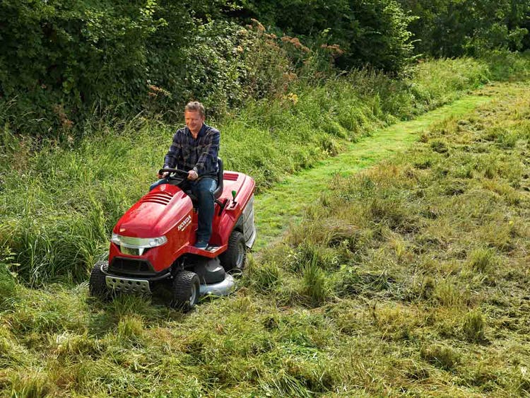 Mann sitzt auf Honda HF 2317 HM Aufsitzrasenmäher und mäht hohes Gras